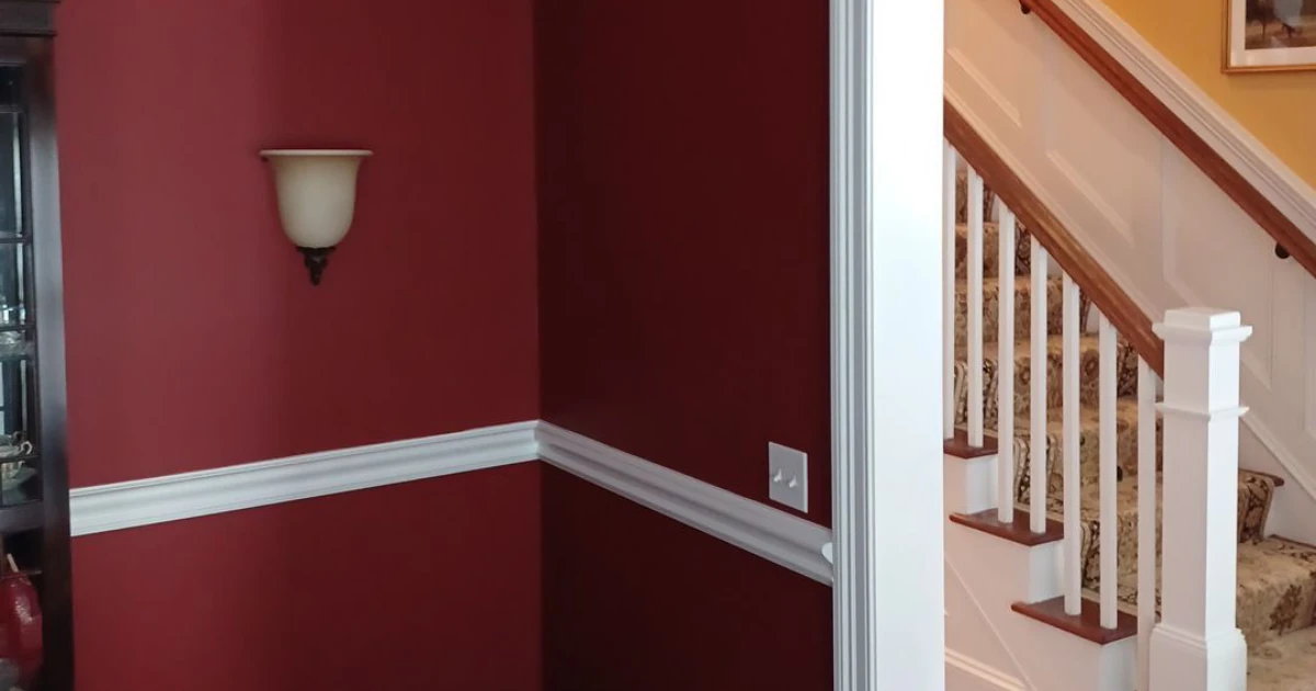 An interior corner painted deep red with white chair-rail trim and a wall sconce, opening onto a staircase with a patterned carpet runner.