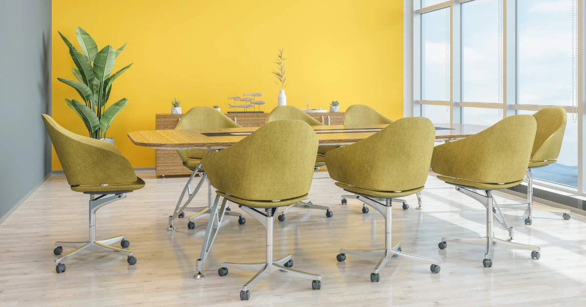 A conference room with a bright yellow accent wall, a wood conference table, mustard-yellow upholstered swivel chairs, and floor-to-ceiling windows.