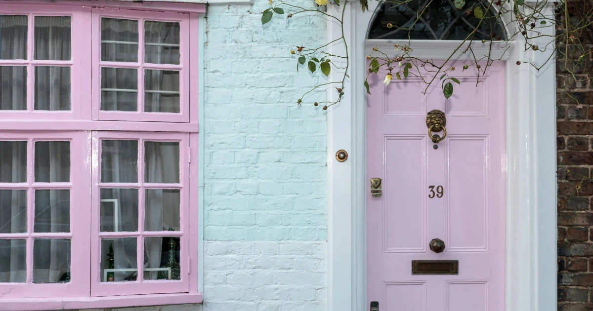 Pale pink front door numbered "39" with a brass lion knocker, matching pink window frames, and mint-green painted brick on a house exterior.