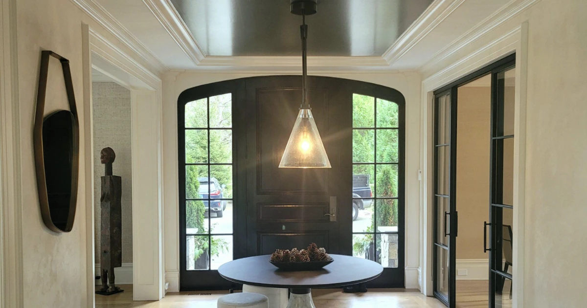 An elegant foyer with a dark-painted front door, arched sidelight windows, a glossy dark tray ceiling, a glass pendant light, and a round table with pinecones.