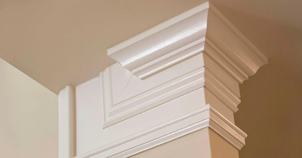 Close-up of crisply painted white crown molding and layered trim at a column corner against tan walls and a tan ceiling.