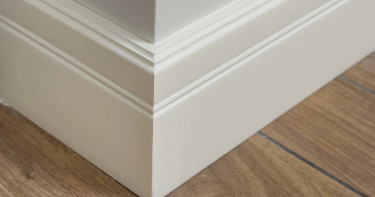 Close-up of crisply painted off-white baseboard trim meeting wood-look plank flooring at an outside corner.