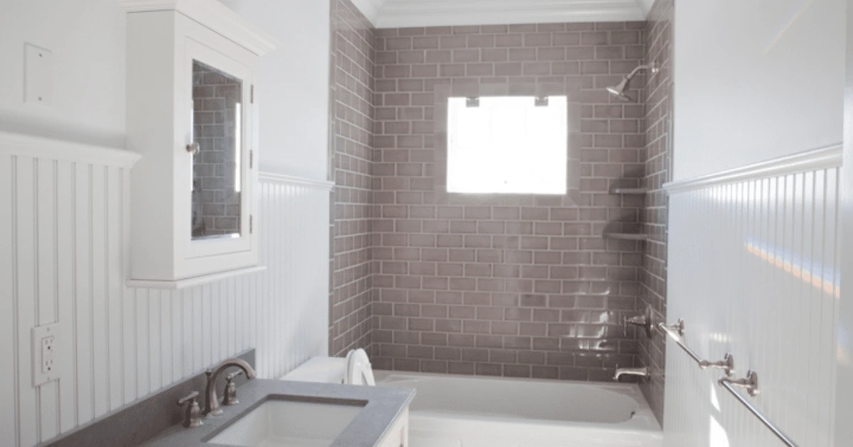 A finished bathroom with a gray subway-tile shower surround over a white tub, white beadboard wainscoting, and a gray vanity countertop below a white mirrored medicine cabinet.