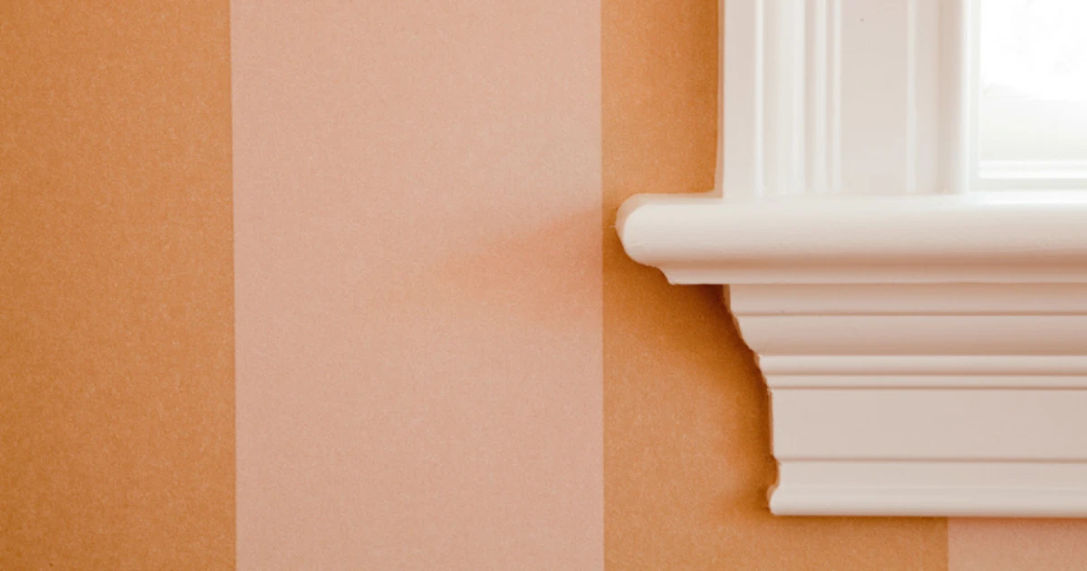 Close-up of a wall painted in wide tone-on-tone peach vertical stripes meeting crisply painted white window trim and sill molding.