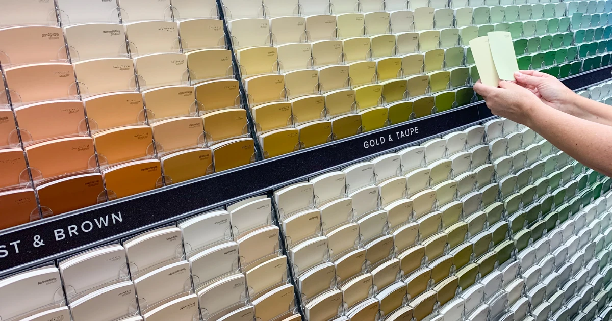 Hand holding paint chips against a display of neutral, gold, and green colors during a color consultation